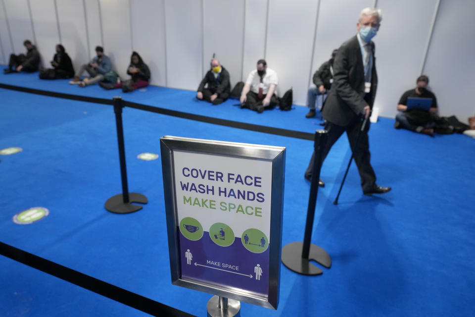 FILE - In this Oct. 29, 2021, file photo, an attendee walks past a warning sign for COVID-19 measures in Glasgow, Scotland. Despite the concerns about the coronavirus from some of the delegates from around the world, the British government decided to hold an in-person conference, arguing that world leaders must act now to prevent catastrophic global warming — and that they will be more effective if they can talk face-to-face. (AP Photo/Matt Dunham)