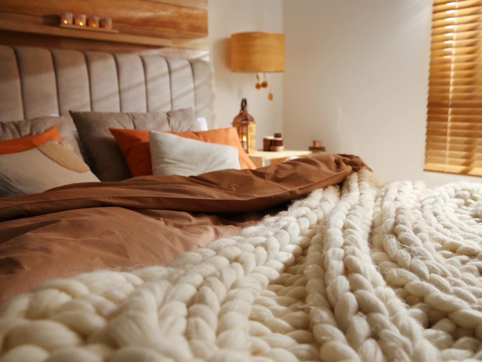 Bed with cozy knitted blanket and cushions