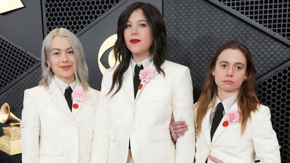 From left: Phoebe Bridgers, Lucy Dacus and Julien Baker of Boygenius in matching cream-colored Thom Browne suits with red pins and carnations on their lapels. - Jordan Strauss/Invision/AP