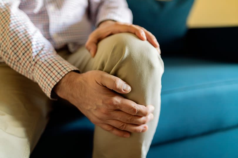 A man grips his lower thigh and upper calf with his hands