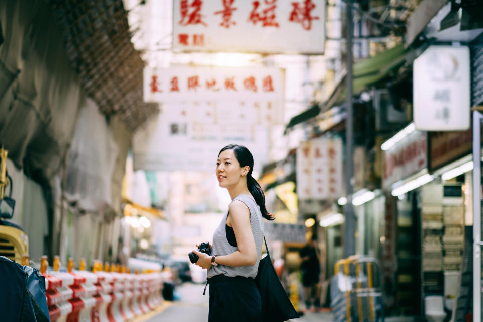 A woman carrying a camera, exploring and walking through local city street. (PHOTO: Getty Images)