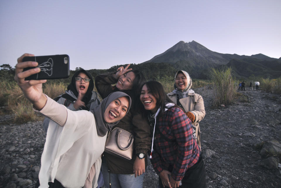 In this Tuesday, Aug. 6, 2019, photo, local tourists take a selfie with the background of Mount Merapi, in Yogyakarta, Indonesia. The Indonesian city of Yogyakarta and its hinterland are packed with tourist attractions, including Buddhist and Hindu temples of World Heritage. Yet many tourists still bypass the congested city and head to the relaxing beaches of Bali. Recently re-elected President Joko Widodo wants to change this dynamic by pushing ahead with creating "10 new Balis," an ambitious plan to boost tourism and diversify South Asia's largest economy. (AP Photo/Slamet Riyadi)
