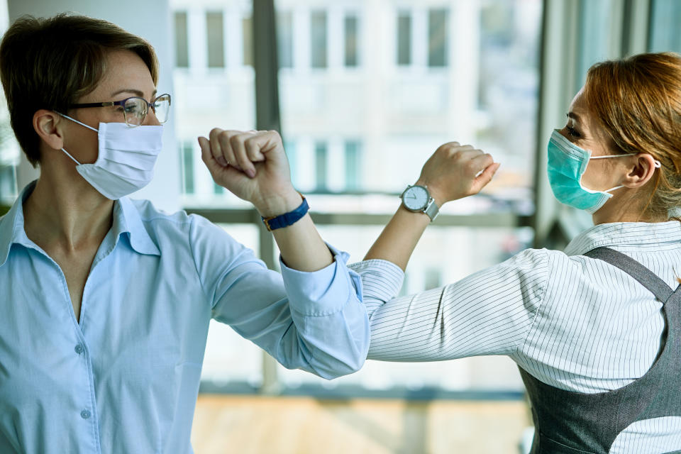 Two businesswomen elbow bumping while greeting each other in the office during COVID-19 epidemic.