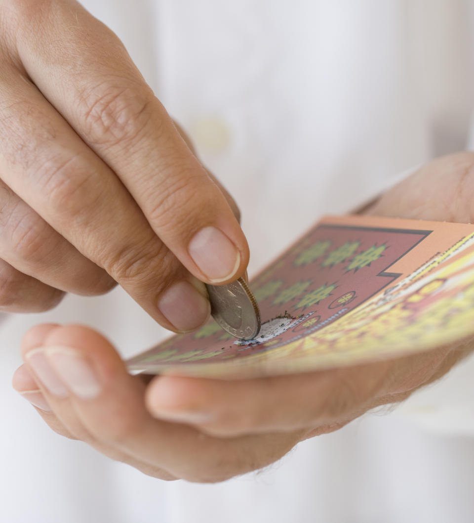 A close-up of a person's hand using a coin to scratch a lottery ticket