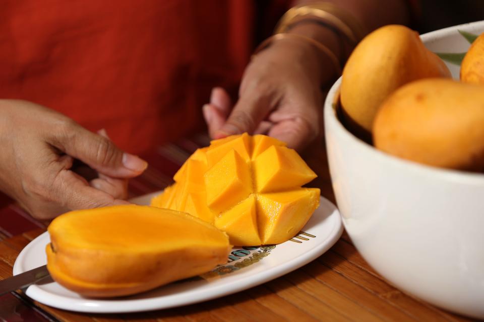 Helen Castillo holds a side of a mango after cutting it into cubes. Thursday, July 21, 2022