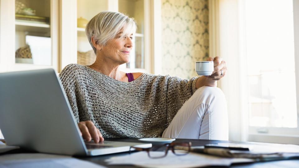 Pensive woman looking away drinking tea at laptop.