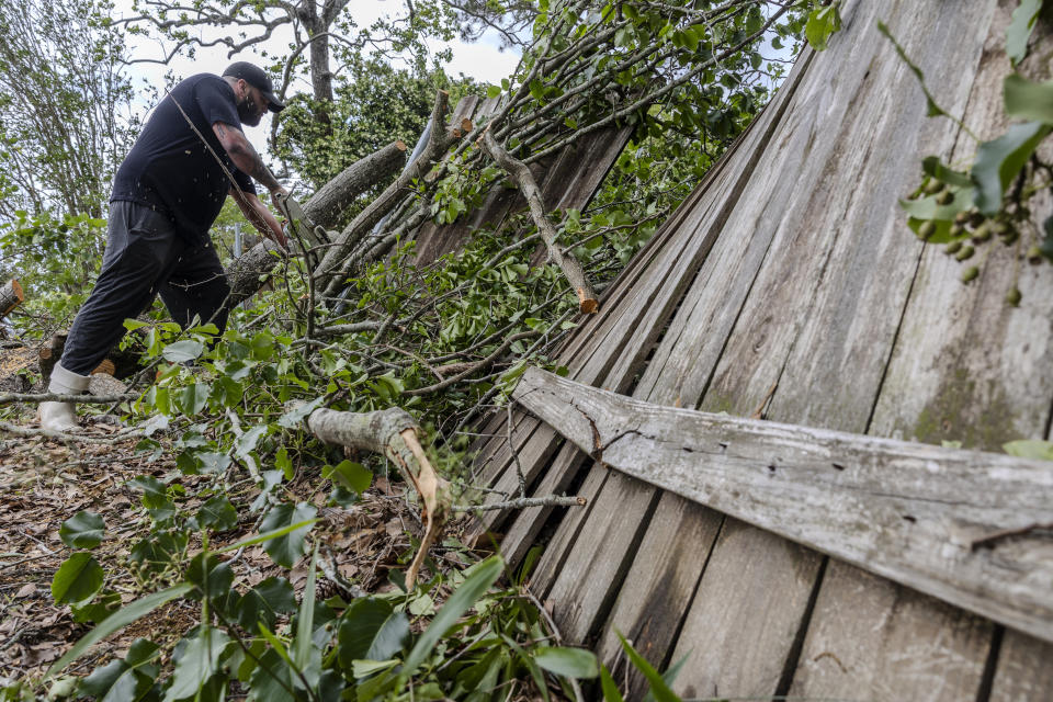 Joe Morehouse saws trees off the side of his house and fence on Thursday, April 11, 2024, the day after a tornado hit parts of Slidell, La. (Chris Granger/The Times-Picayune/The New Orleans Advocate via AP)