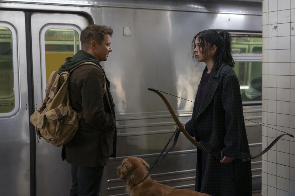 Jeremy Renner and Hailee Steinfeld stand on a subway platform.