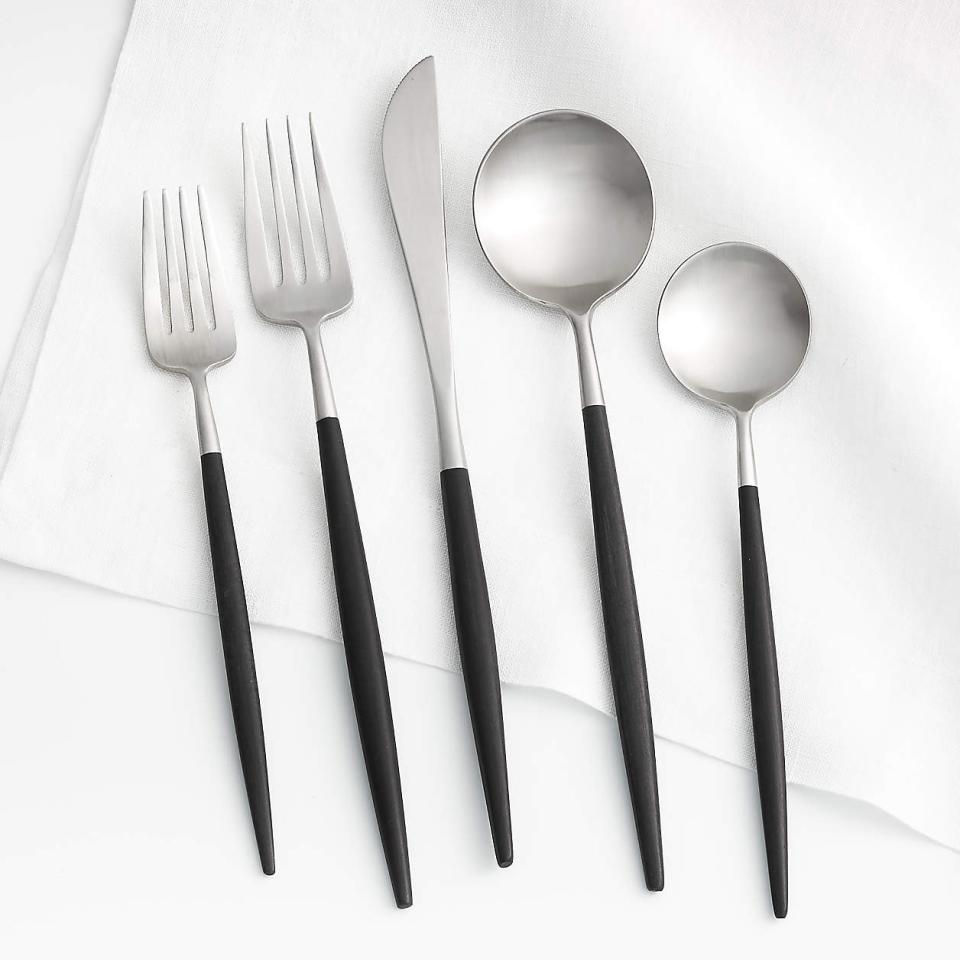 Five pieces of silverware with black handles and silver tops on white backdrop