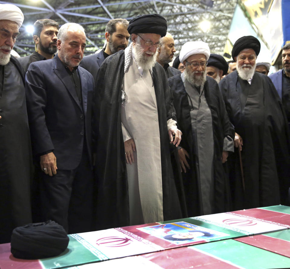 In this photo released by the office of the Iranian supreme leader, Supreme Leader Ayatollah Ali Khamenei, center, leads a prayer over the flag-draped coffins of the late President Ebrahim Raisi and his companions who were killed in a helicopter crash on Sunday in a mountainous region of the country's northwest, at the Tehran University campus, during a funeral ceremony for them in Tehran, Iran, Wednesday, May 22, 2024. (Office of the Iranian Supreme Leader via AP)