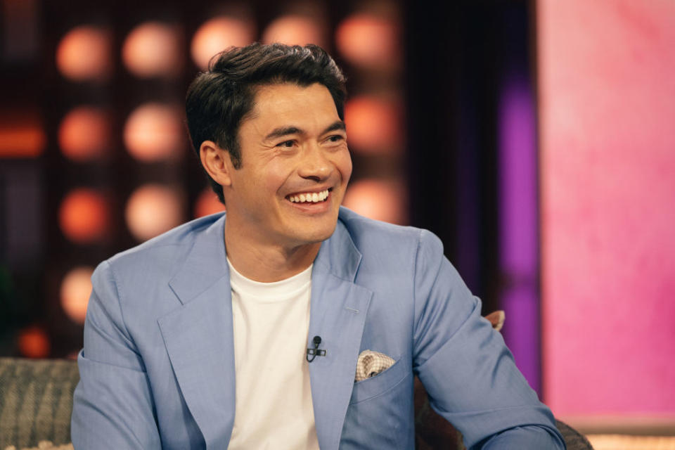 Henry Golding smiling during an interview, wearing a blue blazer and white shirt