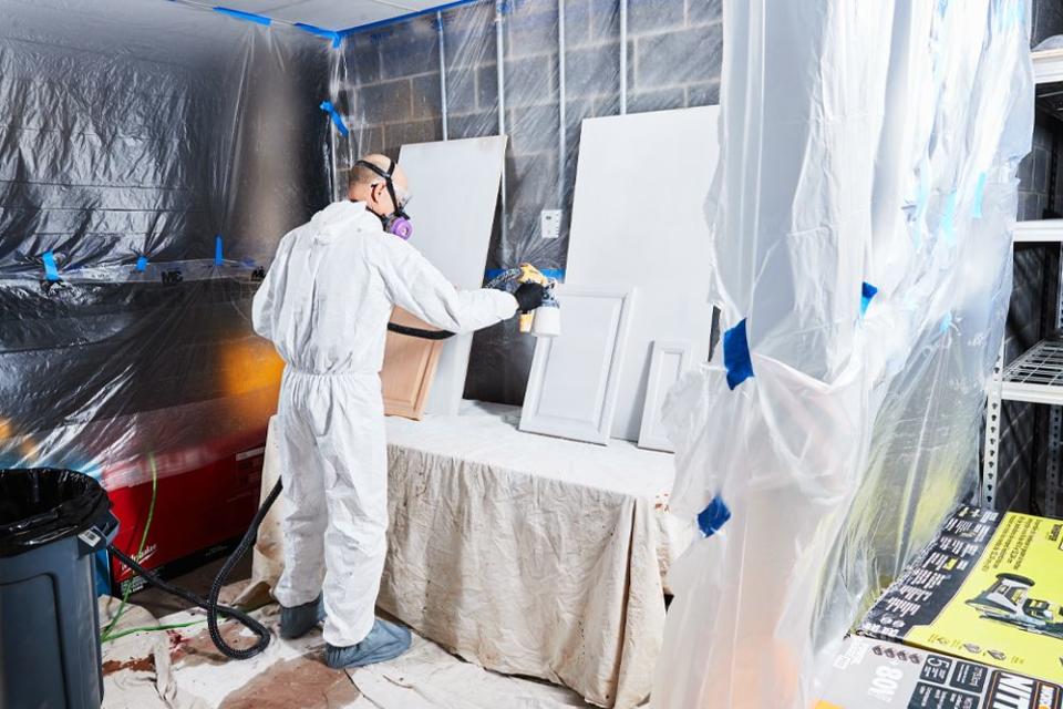 a man using his homemade spray booth to spray paint parts of his kitchen cabinets