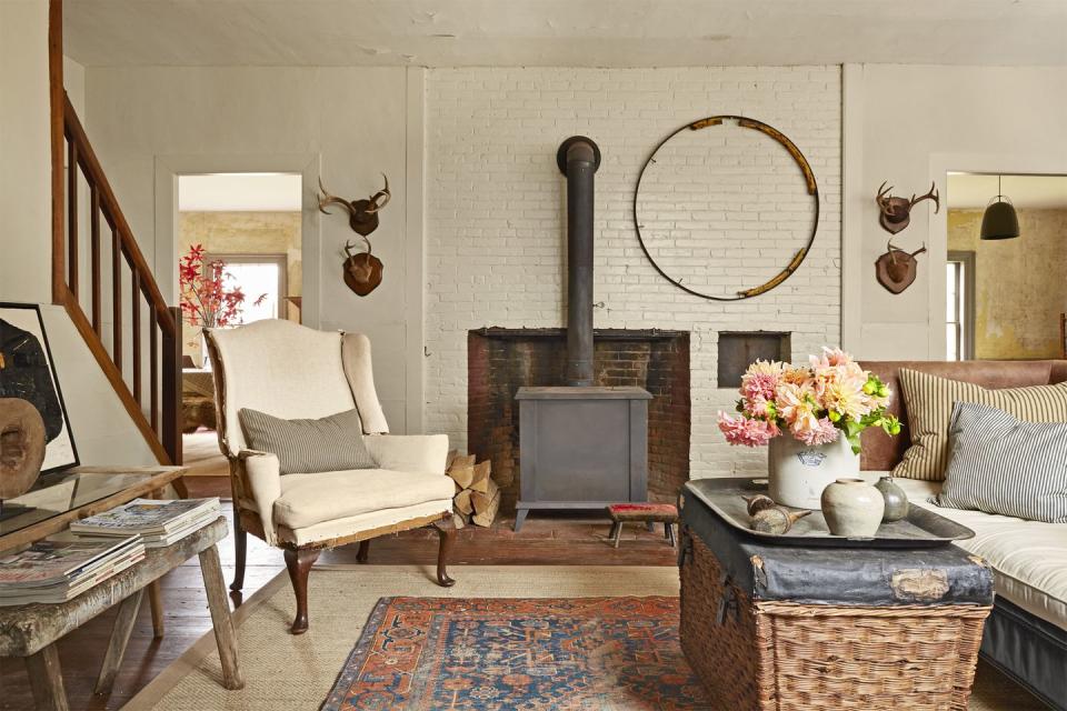 living room with brown white paint, antique upholstered wingback chair, rumpled sofa, wood burning fireplace