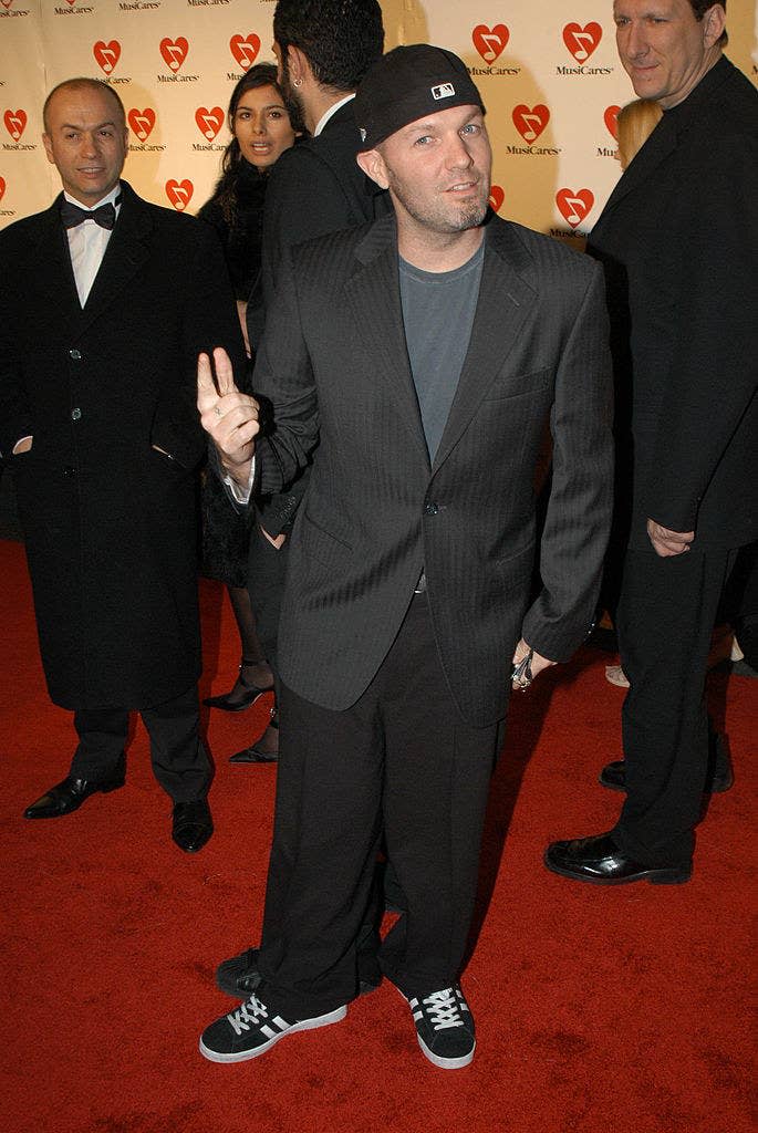 Fred wearing a suit with a tee-shirt, sneakers, and a baseball cap worn backwards on a red carpet