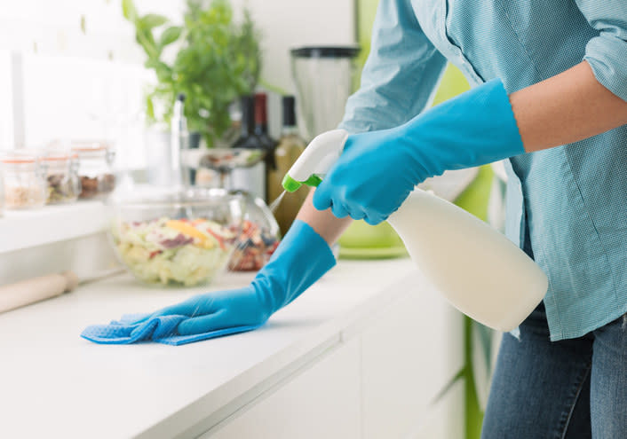 Person wearing gloves and spraying a kitchen countertop