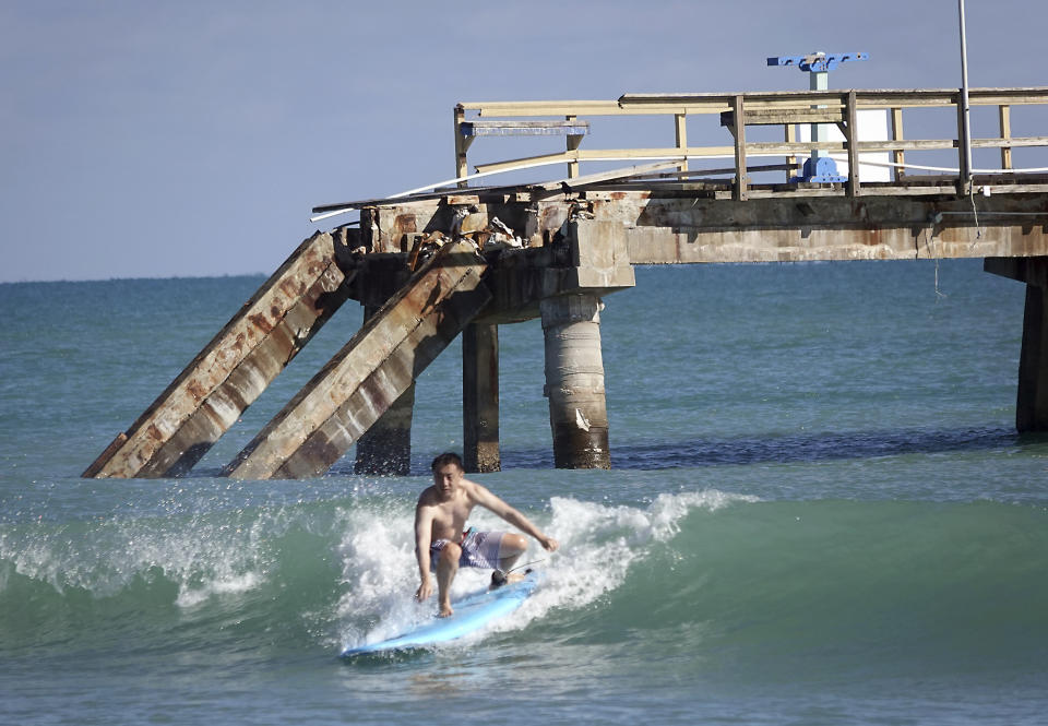 More pieces of Anglin's Fishing Pier in Lauderdale-by-the-Se, Fla., a were washed into the Atlantic Ocean by the weekend's passing storm, as a man surfs in front of it, Monday, Dec. 18, 2023. The pier was rendered inoperable by Hurricane Nicole in early November 2022. (Joe Cavaretta/South Florida Sun-Sentinel via AP)