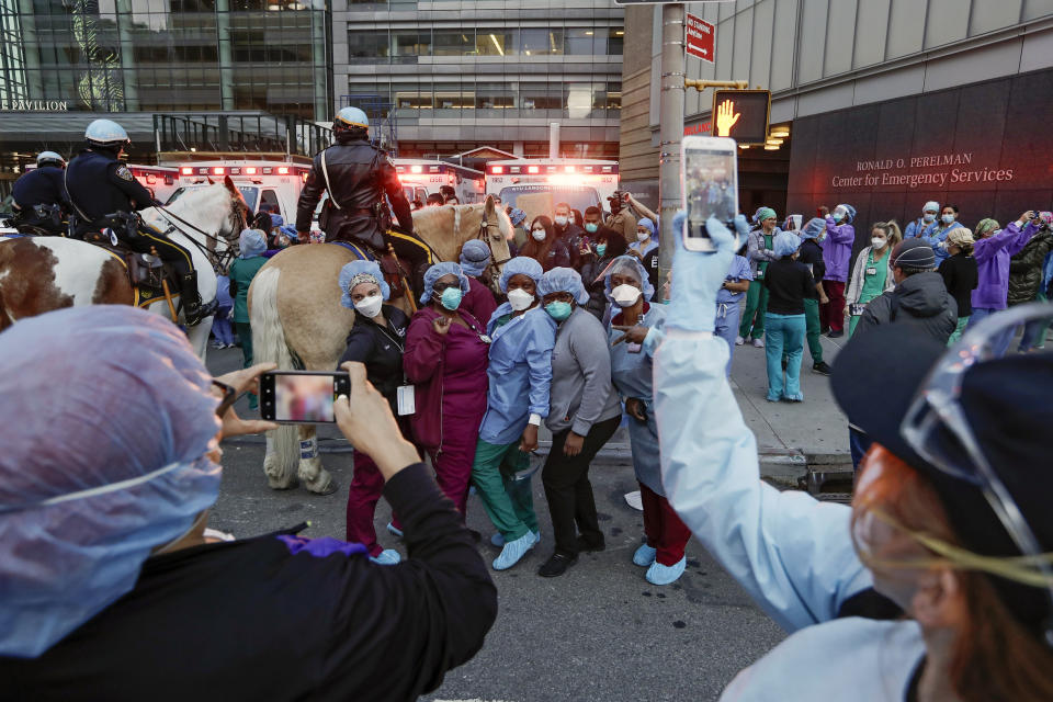 Medical workers pose for photographs as police officers and pedestrians cheer for them outside NYU Medical Center Thursday, April 16, 2020, in New York. (AP Photo/Frank Franklin II)