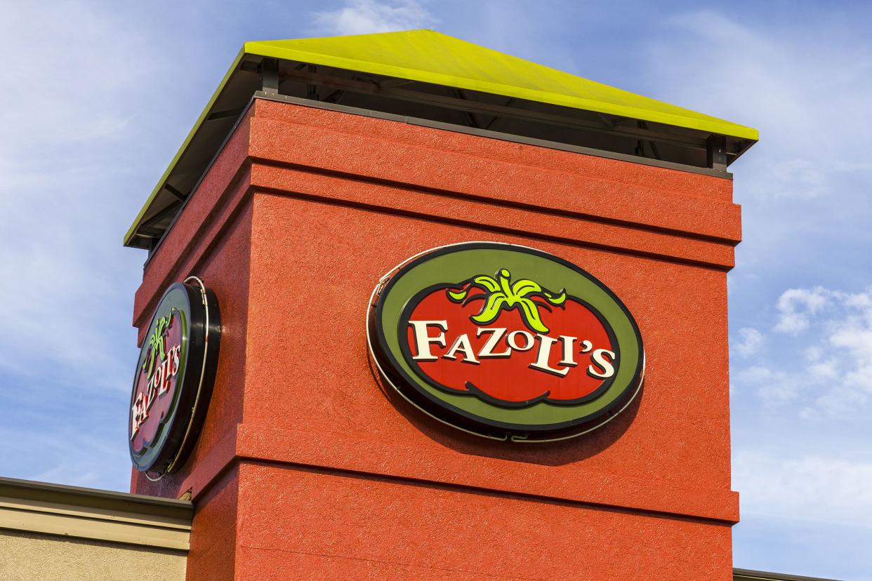 Sign on top front of Fazoli's restaurant, Kokomo, Indiana, brick red stucco tower, against a blue sky with white clouds