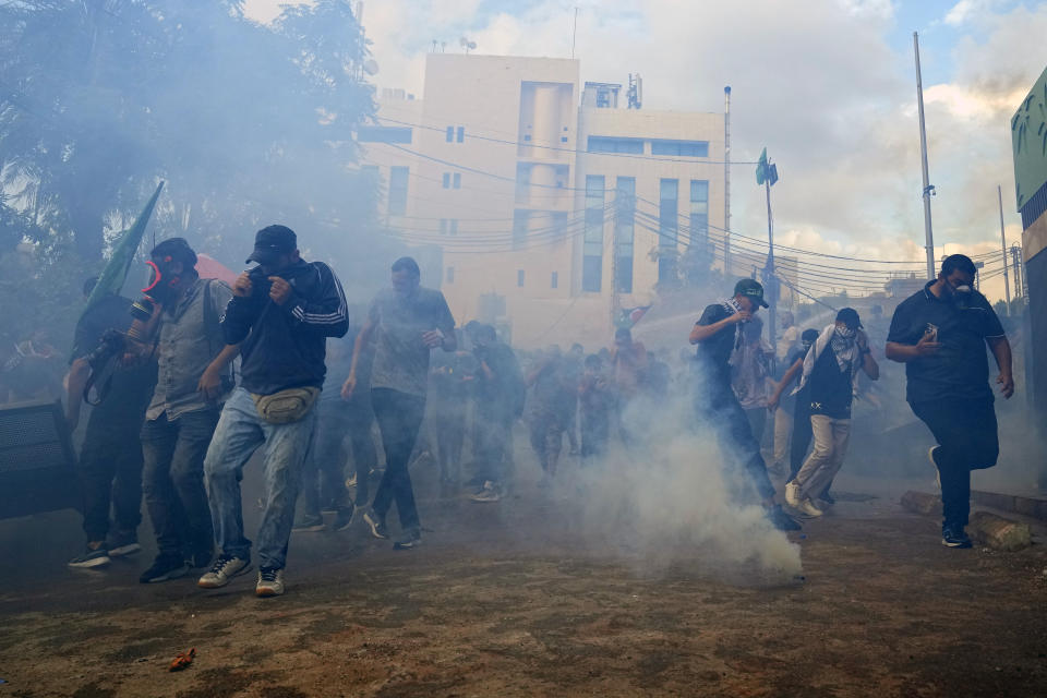 Protesters take cover from tear gas fired by riot police during a demonstration in solidarity with the Palestinian people in Gaza, near the U.S. embassy in Aukar, a northern suburb of Beirut, Lebanon, Wednesday, Oct. 18, 2023. Hundreds of angry protesters are clashing with Lebanese security forces in the Lebanese suburb Aukar near the United States Embassy. (AP Photo/Bilal Hussein)