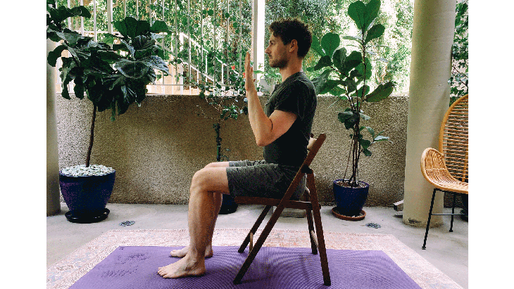 Man seated on a chair practicing Chaturanga, or a half push-up, without any weight on his wrists or shoulders