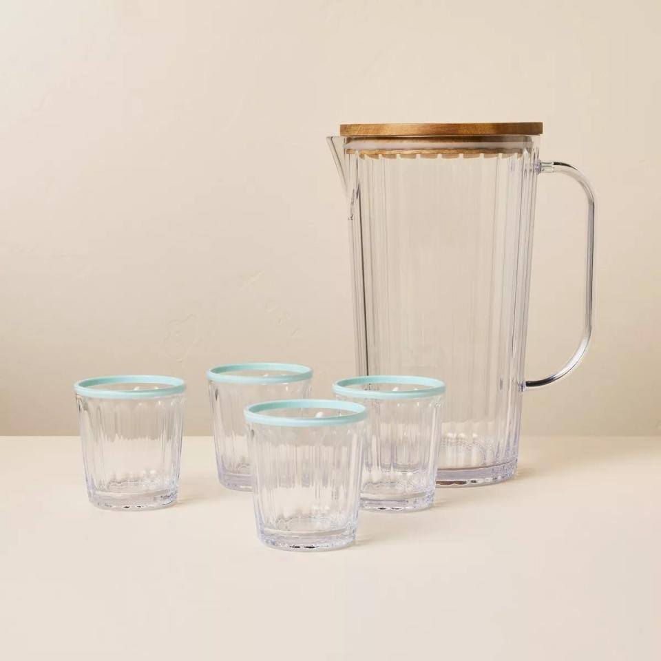 Glass pitcher and four matching glasses with a hint of blue on the rim, on a plain surface