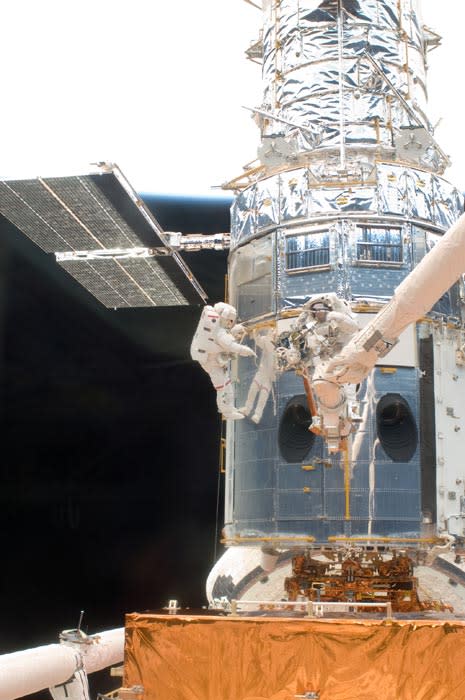 A metal-wrapped spacecraft can be seen up close.  Astronauts maintain it.