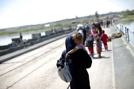 An Iraqi woman carries a girl as she walks along a pontoon bridge over the Tigris river on the outskirts of Hammam al-Alil, south of Mosul, Iraq, April 17, 2017. REUTERS/Andres Martinez Casares