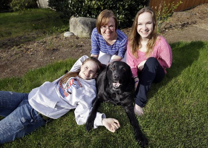 In this photo taken Sunday, April 28, 2013, Kelly Dempsey, center sits with daughters Jordan, left, and Erin Barker, both 17, and their dog Alou, 9, at their home in Bothell, Wash. In Seattle 10 years ago, a dog named Jeeter became the first professionally trained dog to help a child testify, assisting the twins as they were getting ready to testify against the father they said molested them. Dogs have helped thousands of victims and witnesses since, but some challenges are working their way through the courts, driven by attorneys who claim the dogs are distractions or sympathy magnets. So far, all lower courts have upheld the use of dogs. (AP Photo/Elaine Thompson)