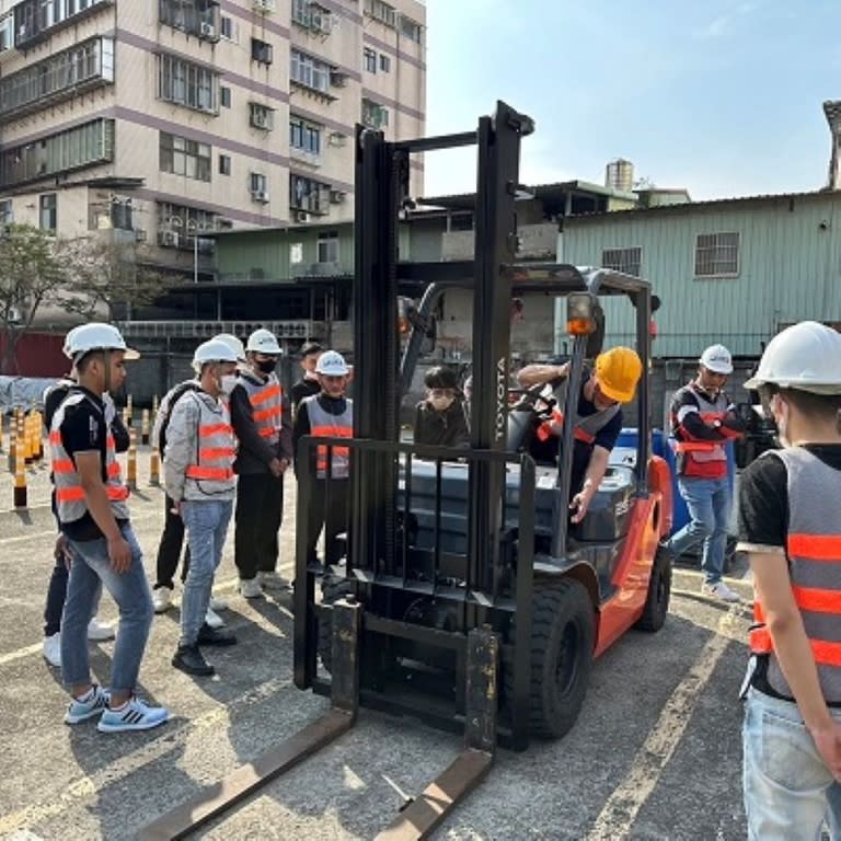 《圖說》光啟高中汽車科教師(黃帽)示範，翻譯(黑衣)即時口譯，15位學員認真看示範。〈勞工局提供〉