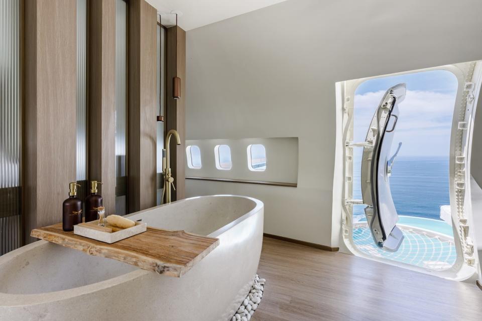 A bath tub sits inside of a plane. The side door of the plane is open, overlooking a pool.