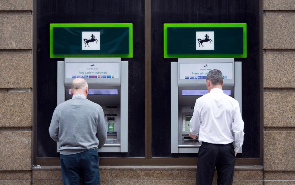 Customers stop to use automated teller machines outside a Lloyds bank branch