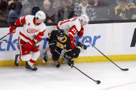 Boston Bruins left wing Brad Marchand (63) falls to the ice as he passes out from the boards ahead of Detroit Red Wings defenseman Ben Chiarot, left, and center Austin Czarnik (21) during the first period of an NHL hockey game, Saturday, March 11, 2023, in Boston. (AP Photo/Mary Schwalm)