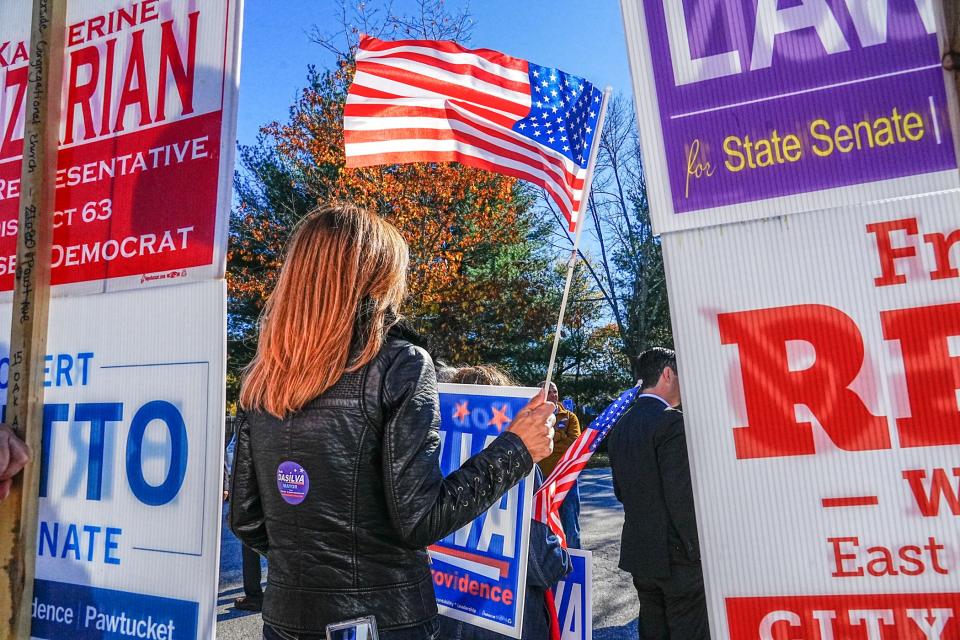 Connie McNally holds a flag outside the polling station at Myron J. Francis Elementary School in East Providence on Tuesday.