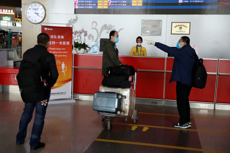 Men wearing face masks speak in front of an information counter at Beijing Capital International Airport