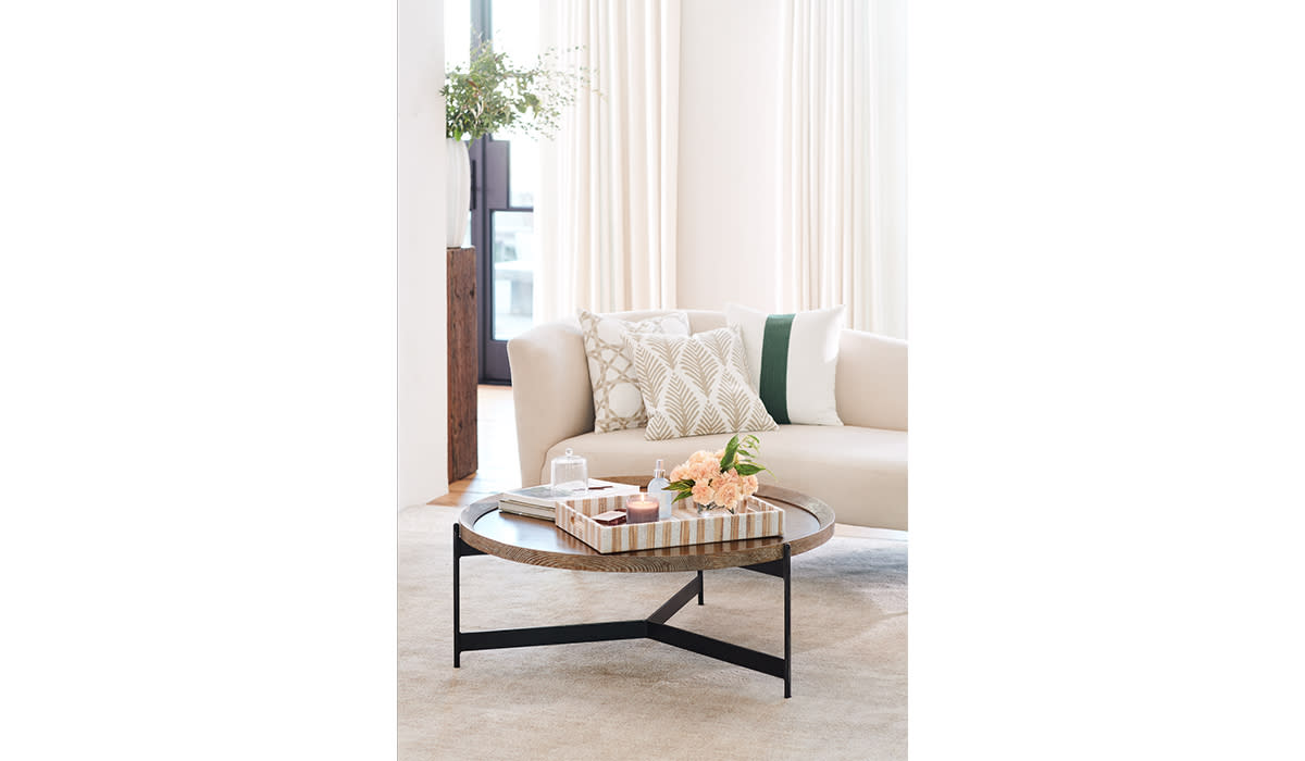 Neutral sofa with three different patterned pillows arranged in the corner with a coffee table in front of it