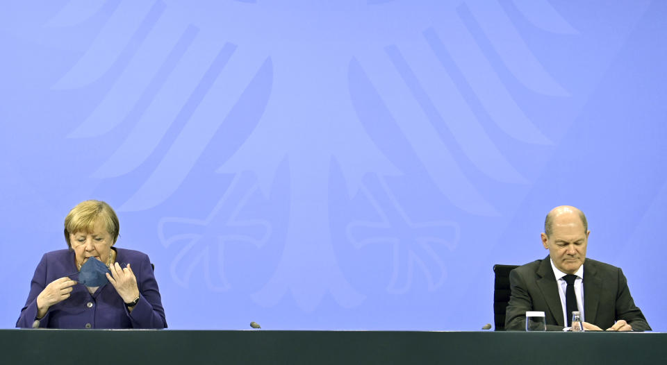 German Chancellor Angela Merkel, left, removes her face mask as she arrives to give a press conference together with Finance Minister Olaf Scholz, following a meeting with the heads of government of Germany's federal states at the Chancellery in Berlin, Thursday, Dec. 2, 2021. Merkel said Thursday that people who aren't vaccinated will be excluded from nonessential stores, cultural and recreational venues, and parliament will consider a general vaccine mandate, as part of an effort to curb coronavirus infections that again topped 70,000 newly confirmed cases in a 24-hour period. (John Macdougall/Pool Photo via AP)