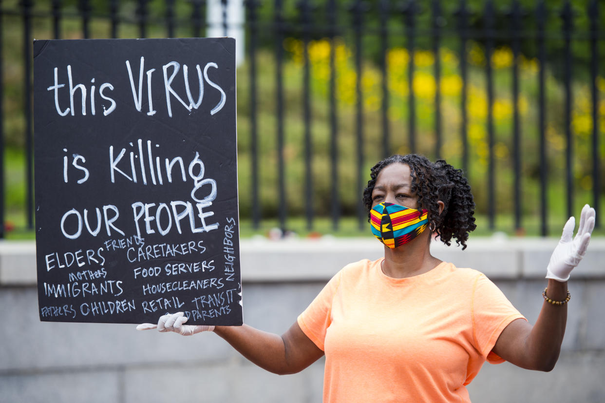 Alice Gaskins holds sign that says "This Virus is Killing Our People" in front of the Massachusetts State House as people representing a number of Black and Latinx organizations perform a "funeral procession" for essential workers that have been sick with or died from COVID-19. (Photo by Blake Nissen for The Boston Globe via Getty Images)