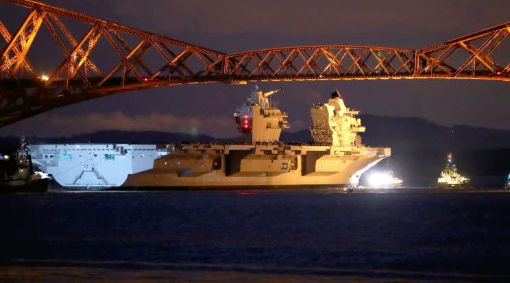 HMS Queen Elizabeth, one of two new aircraft carriers for the Royal Navy, is pulled by tugs under the Forth Rail Bridge in the Firth of Forth on Monday night (PA)