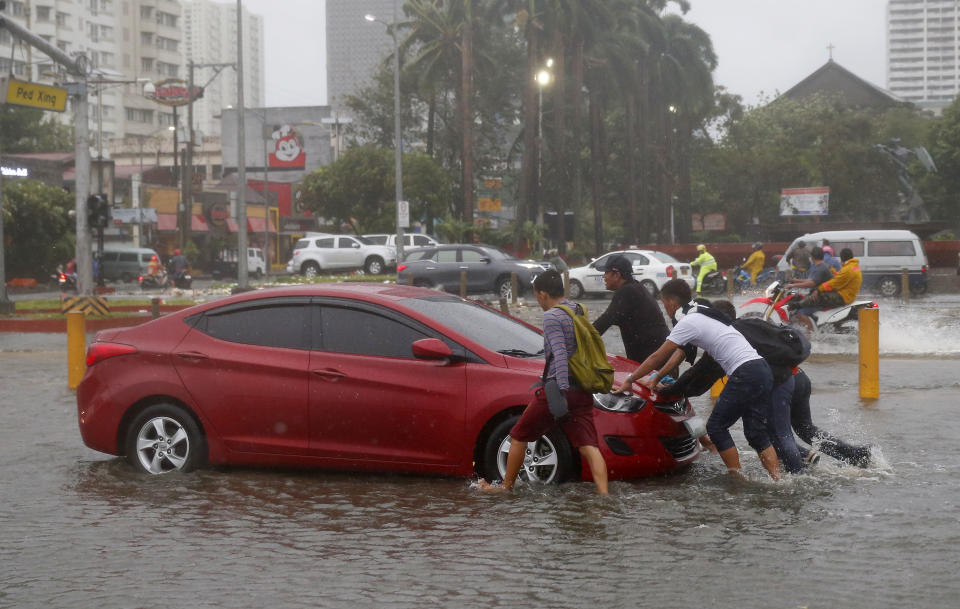 Commuters push a car after it got stuck in the floods due to Typhoon Mangkhut which barreled into northeastern Philippines before dawn Saturday, Sept. 15, 2018 in Manila, Philippines. The typhoon slammed into the Philippines' northeastern coast early Saturday, its ferocious winds and blinding rain ripping off tin roof sheets and knocking out power, and plowed through the agricultural region at the start of the onslaught. (AP Photo/Bullit Marquez)