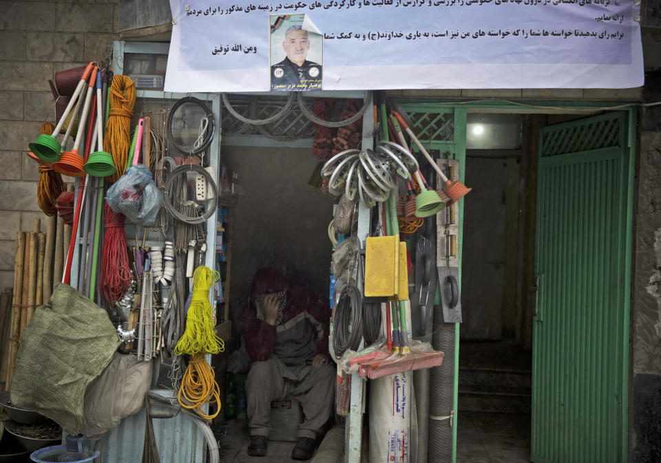 In this Sunday, March 16, 2014 photo, an Afghan shopkeeper hides from pouring rain inside his makeshift store decorated with a picture of Afghan provincial candidate Mohammad Aziz Mansor. Warlords, with a violent past have played a role in influencing Afghan politics since a U.S.-led coalition helped oust the Taliban in 2001. But they are emerging to play an overt political role in next month’s presidential elections as President Hamid Karzai leaves the scene. (AP Photo/Anja Niedringhaus)