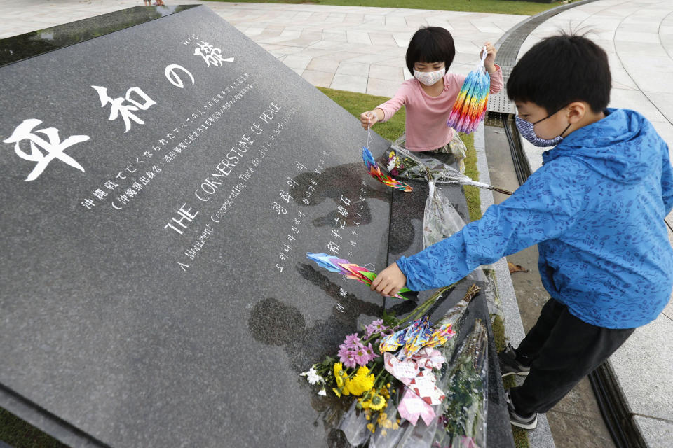 Children place paper cranes at the "Cornerstone of Peace" monument at the Peace Memorial Park in Itoman, Okinawa, Japan, Tuesday, June 23, 2020. Okinawan people find it unacceptable that their land is still occupied by a heavy U.S. military presence even 75 years after World War II. They have asked the central government to do more to reduce their burden, and Prime Minister Shinzo Abe's government repeatedly say it is mindful of their feelings, but the changes are slow to come. (Kyodo News via AP)