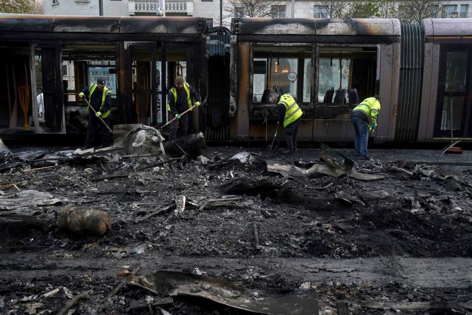 Debris is cleared from a burned out Luas and bus on O'Connell Street, in the aftermath of violence in the city center on Thursday evening, in Dublin, Friday, Nov. 24, 2023. The unrest came after an attack on Parnell Square East where five people were injured, including three young children.