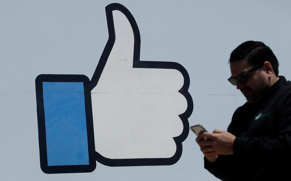 In this April 25, 2019, photo a man walks past the thumbs up Like logo on a sign at Facebook headquarters in Menlo Park, Calif - Jeff Chiu/AP