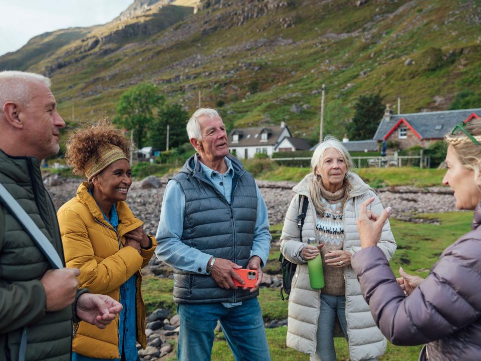 A shot of a group of adults standing on the shore of a sea loch in Torridon, Scotland, chatting.