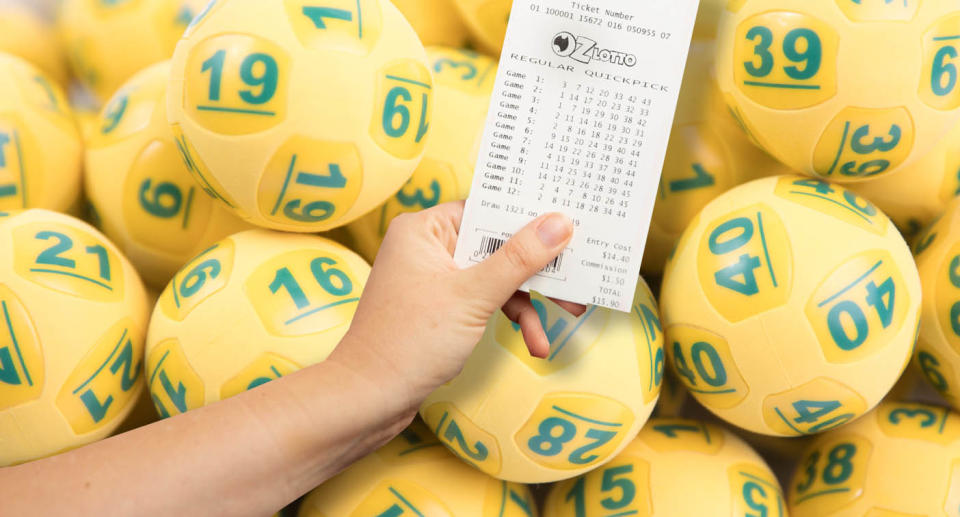 A woman holds an Oz Lotto ticket with Oz Lotto balls in the background.