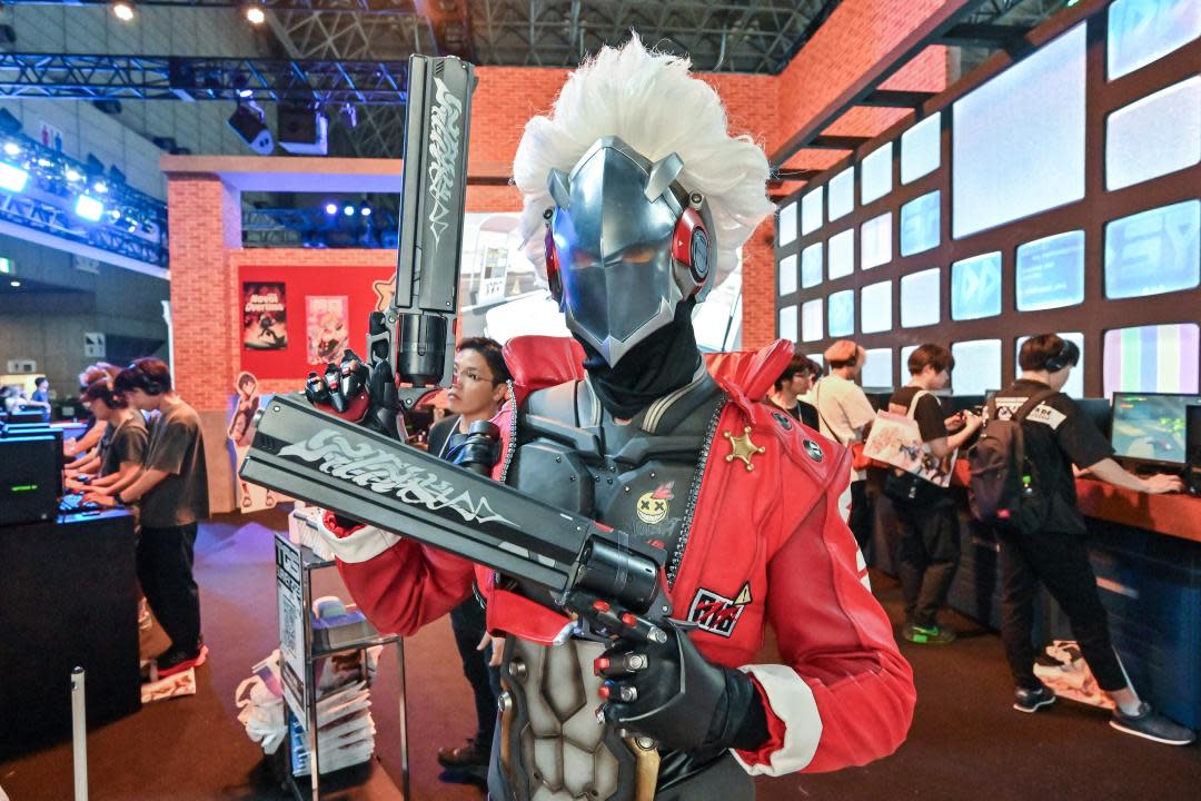 A person posing at a video game show dressed as a character from Zenless Zone Zero surrounded by people playing games.