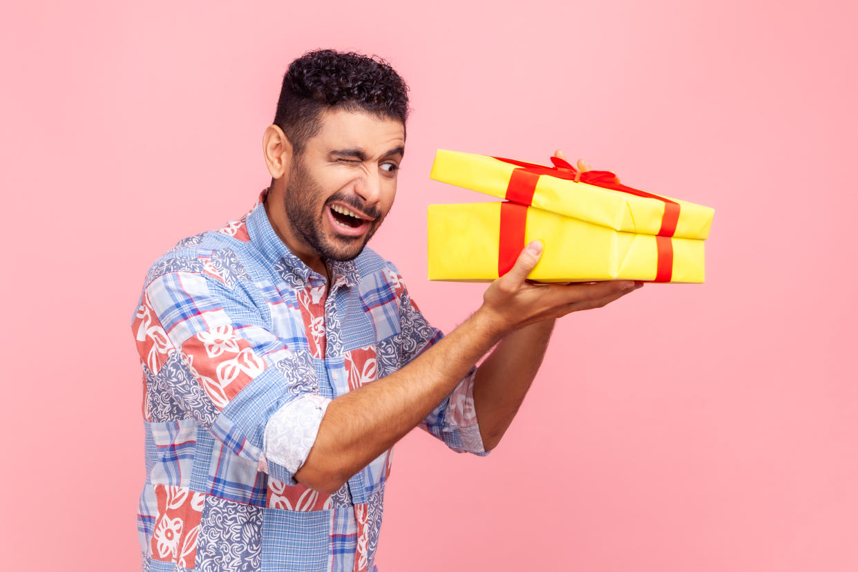 Portrait of curious happy man opening gift, peeking inside box with nosy look, unpacking present, in anticipation of interesting birthday surprise. Indoor studio shot isolated on pink background.