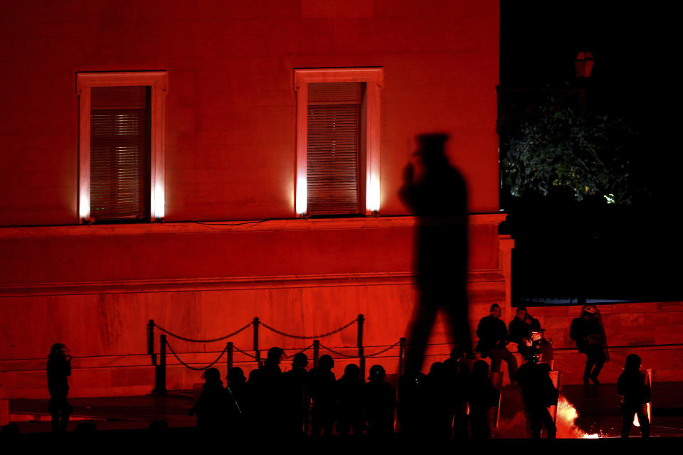 A shadow of a police officer on a wall of parliament and riots police officers stands guard as opponents of Prespa Agreement throw a flare during a rally outside the Greek Parliament in Athens, Thursday, Jan. 24, 2019. Greek lawmakers are debating a historic agreement aimed at normalizing relations with Macedonia in a stormy parliamentary session scheduled to culminate in Friday vote. (AP Photo/Petros Giannakouris)