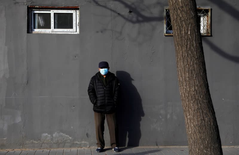 A man wearing a face mask stands along a street in Beijing, China