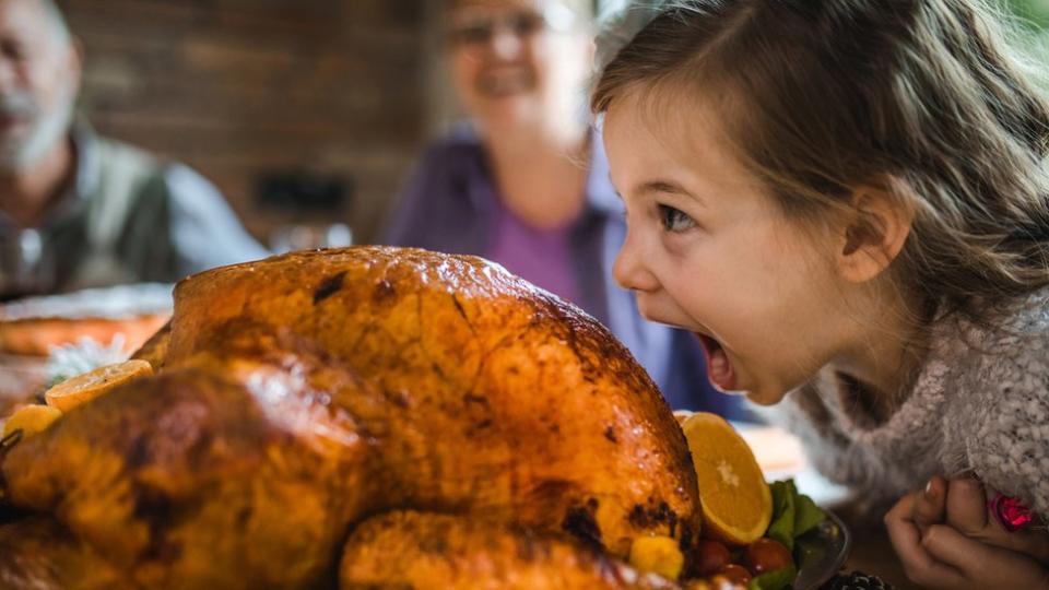 Una niña queriendo dar un mordisco a un pavo asado.